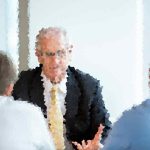 Businessman in a suit speaking to colleagues in a meeting room.