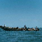 A small boat with several people gliding on calm blue ocean under a clear sky
