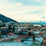 Aerial view of Tbilisi showcasing iconic landmarks and vibrant cityscape under a clear sky.