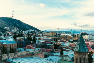 Aerial view of Tbilisi showcasing iconic landmarks and vibrant cityscape under a clear sky.