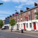 A sunny street view of Georgian-style houses with red doors and a Union Jack flag in Dublin, Ireland.