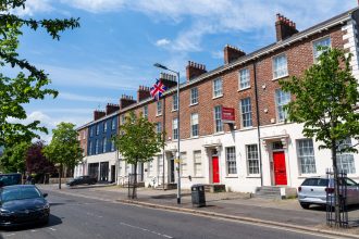 A sunny street view of Georgian-style houses with red doors and a Union Jack flag in Dublin, Ireland.