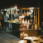 Night market with lit food stalls and people, creating a lively atmosphere.