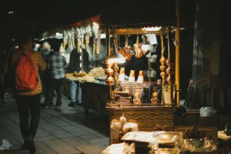 Night market with lit food stalls and people, creating a lively atmosphere.