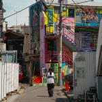 Vibrant urban alleyway in Tokyo with graffiti and lone pedestrian under sunlight.
