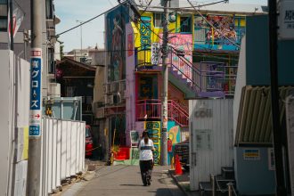 Vibrant urban alleyway in Tokyo with graffiti and lone pedestrian under sunlight.