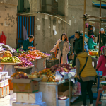 A bustling outdoor market scene filled with colorful fruits and vegetables, and diverse shoppers.