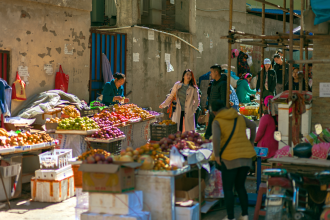 A bustling outdoor market scene filled with colorful fruits and vegetables, and diverse shoppers.